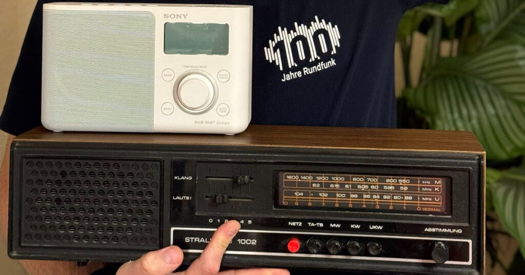 Jan Lehmann mit einen alten und einen neuerem Radio und einen Shirt mit der Aufschrift 100 Jahre Rundfunk